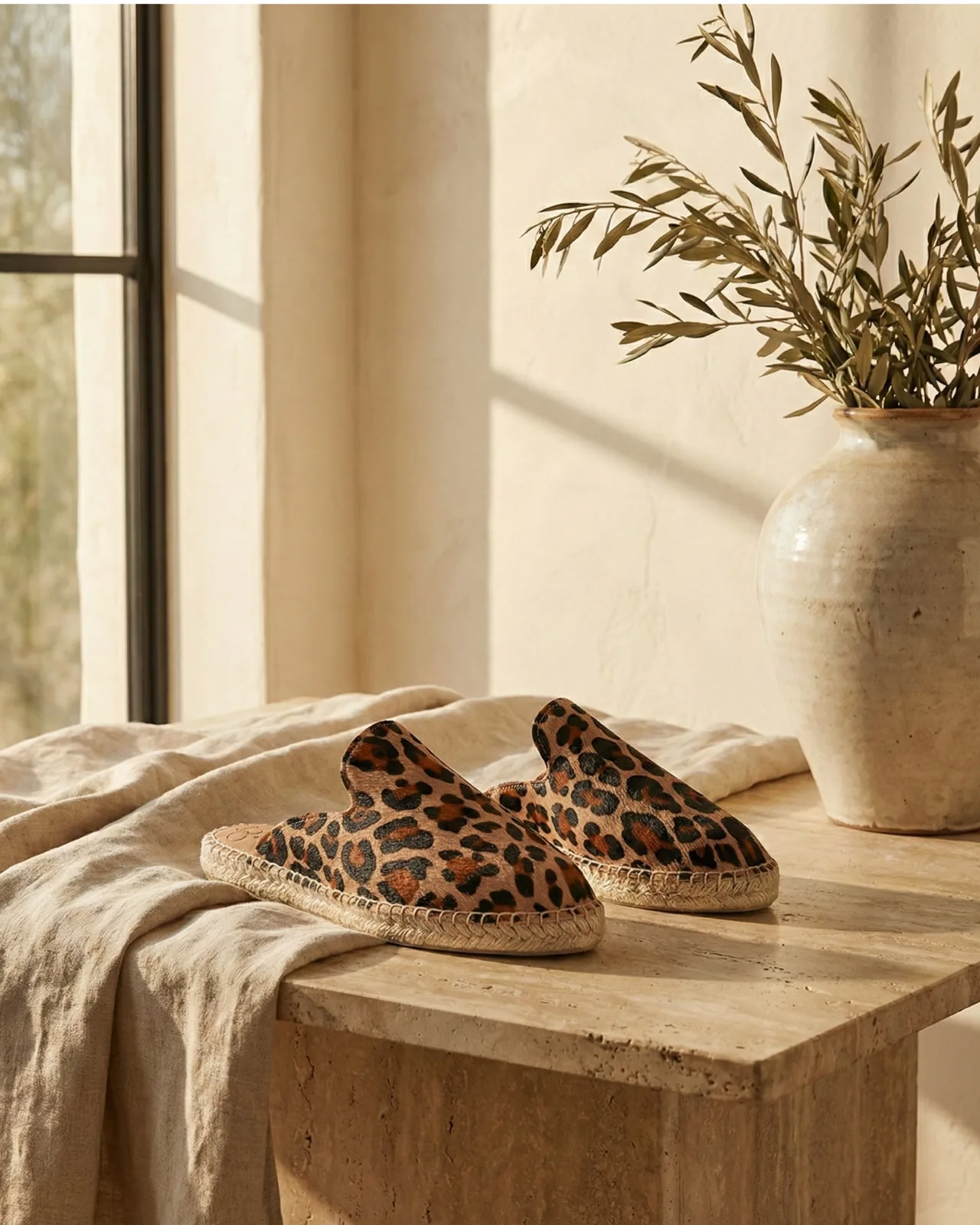 Leopard-print jute-soled mules displayed on a stone table
