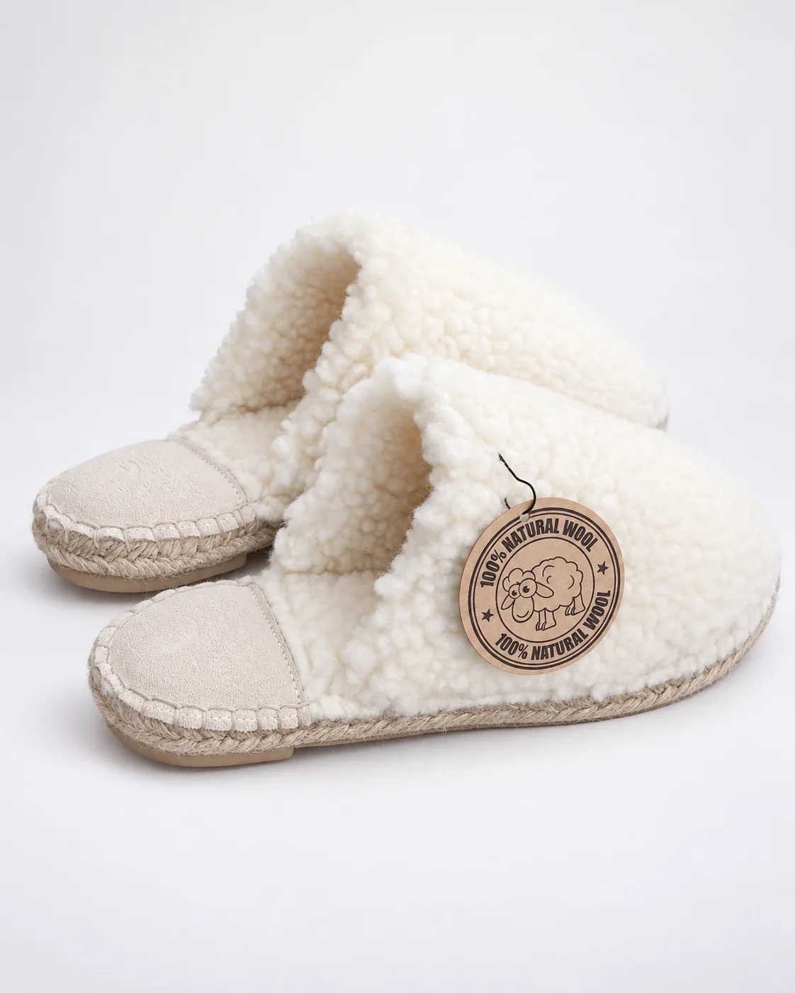 Paire de Dolly Wool en laine bouclée écrue, avec talonnette en cuir velours et semelle de jute cousue, sur fond clair.