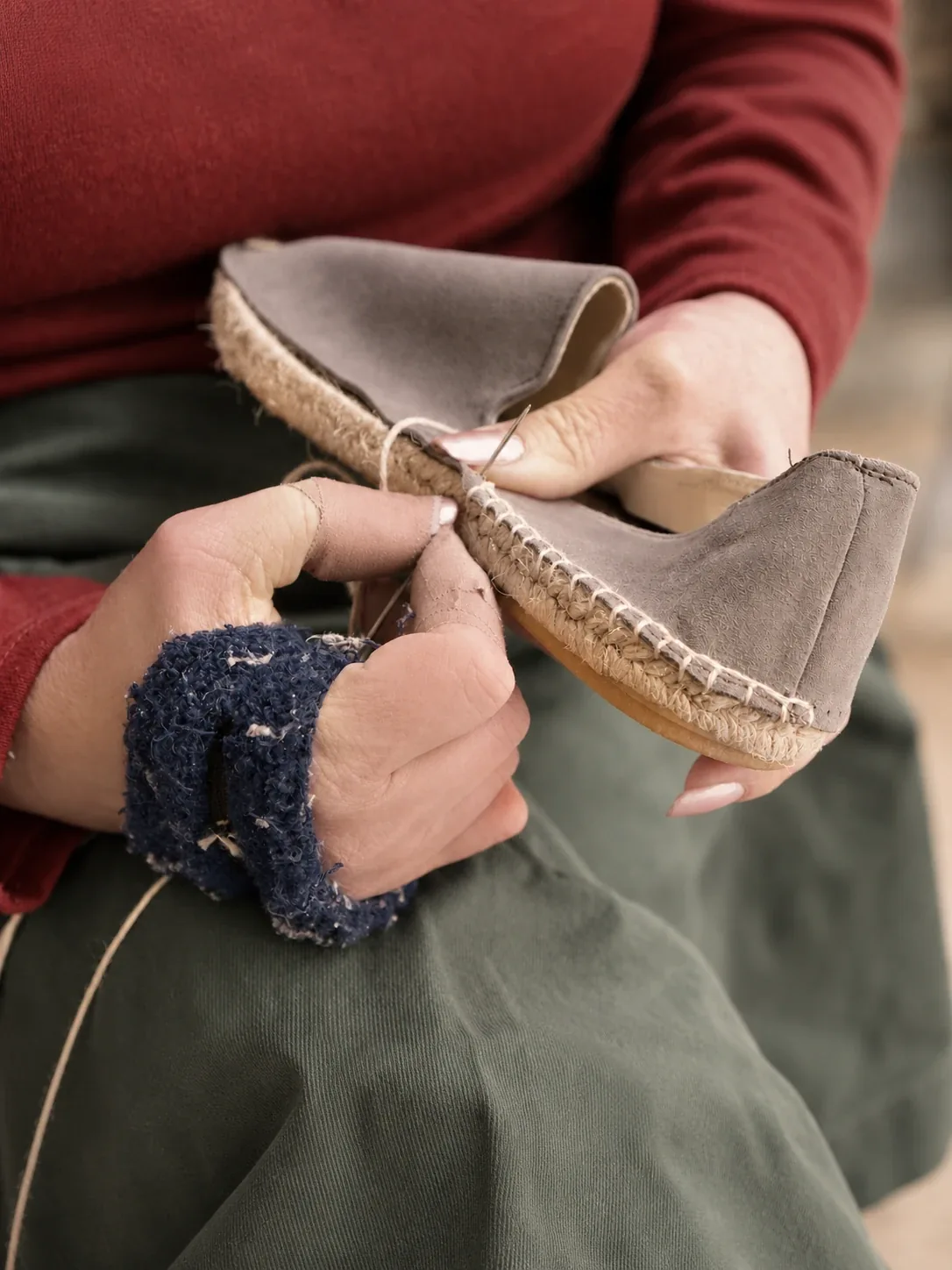 Hands stitching a suede espadrille upper to its jute sole with a needle.
