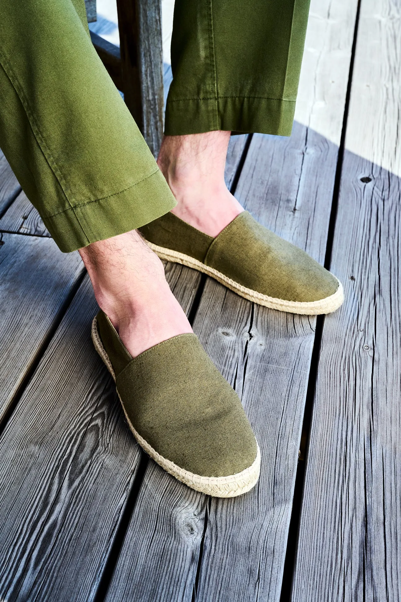 Homme portant des espadrilles en toile kaki sur un ponton en bois.