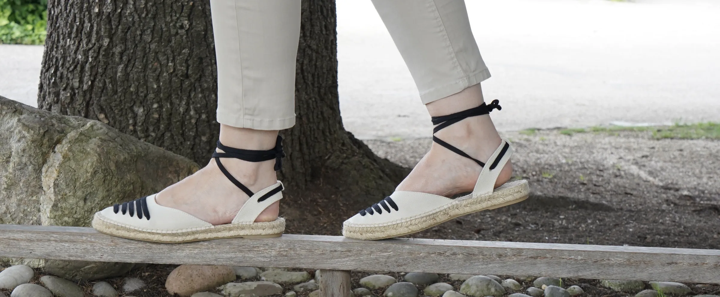 Espadrilles bicolores à liens noirs, portées sur une rambarde en bois.