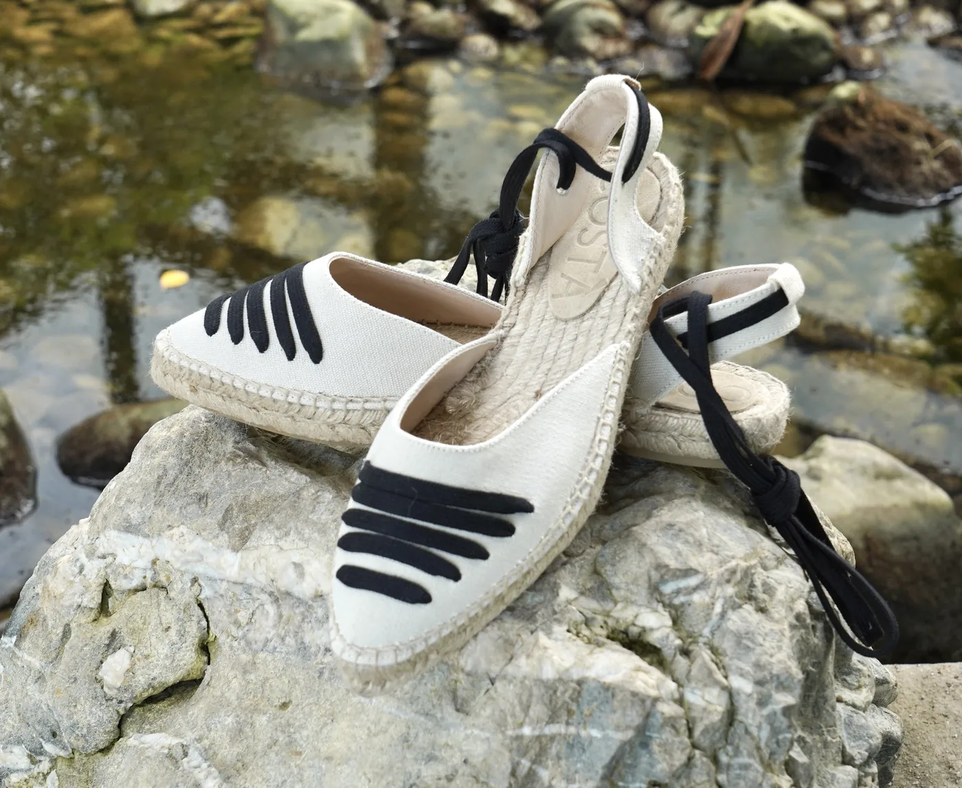 Paire d’espadrilles écrues et noires à liens, posée sur une pierre.