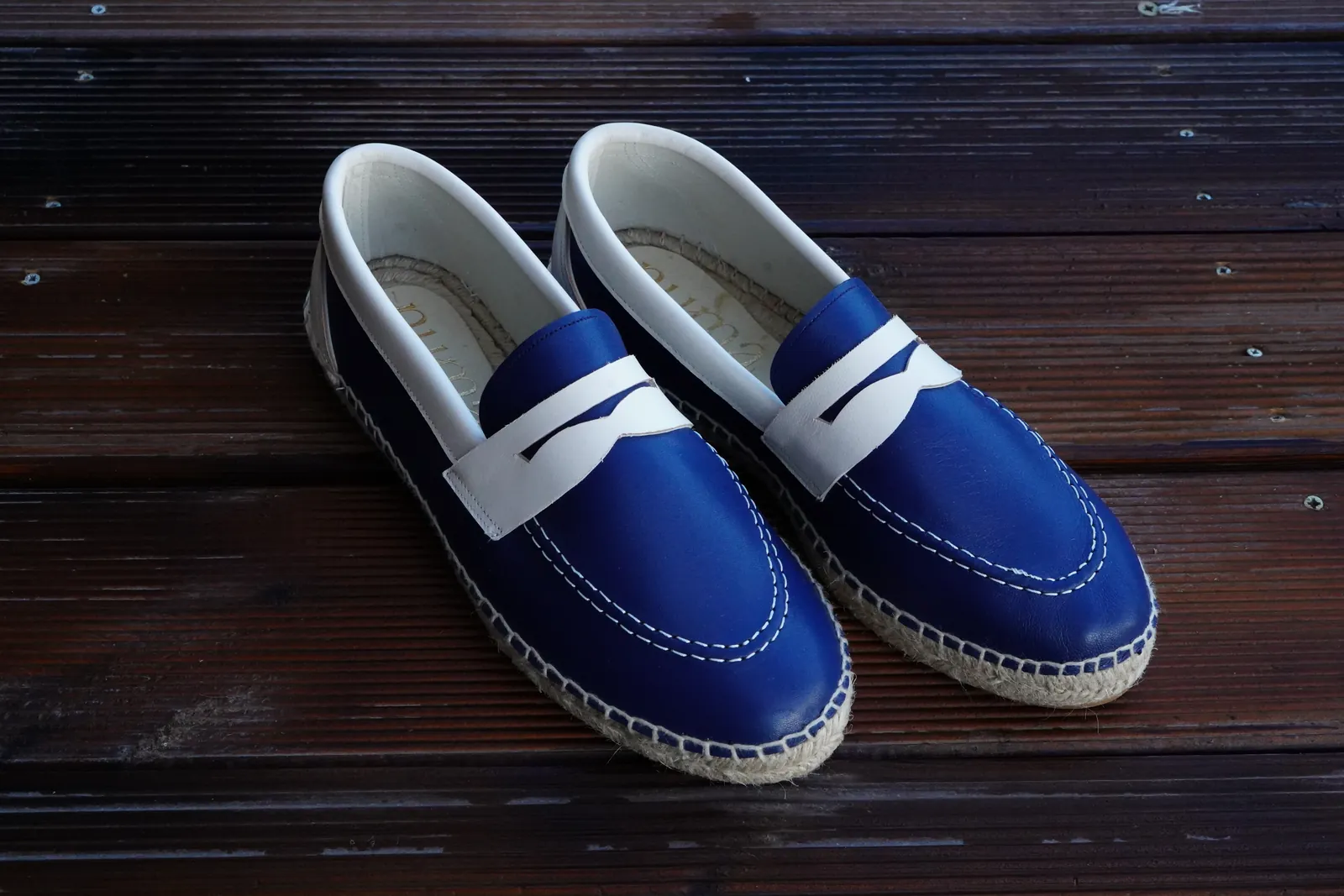 Blue and white loafers with rope soles on a wooden table.