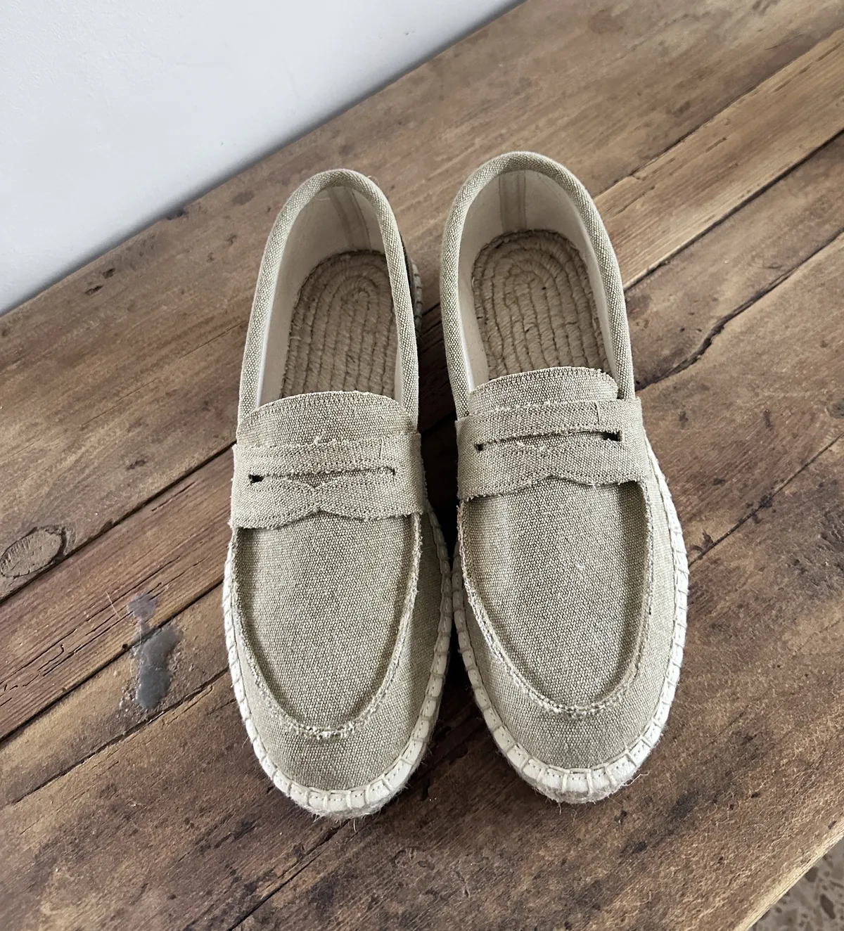 Light canvas loafers with rope soles, seen from above on wood.