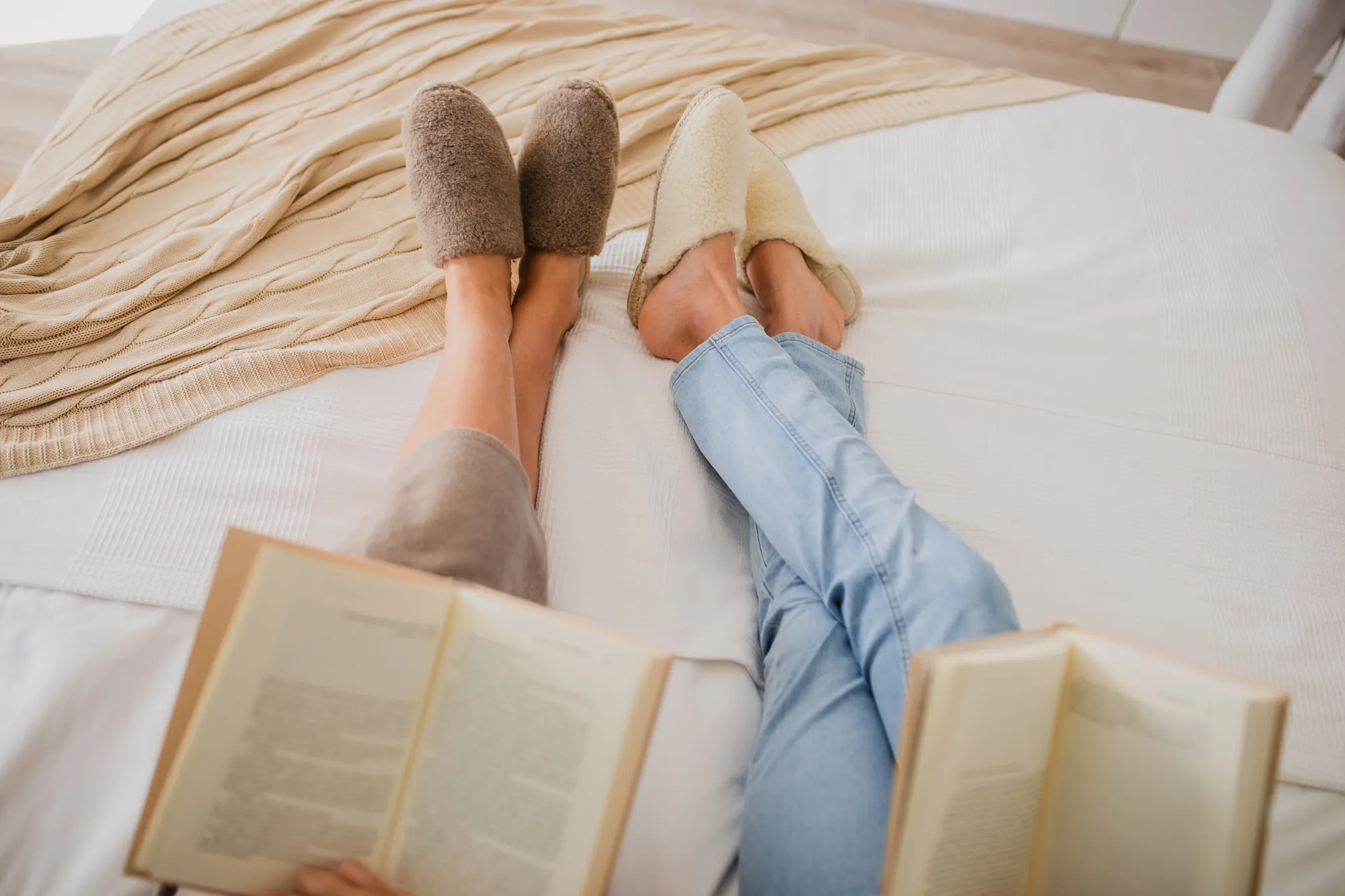 Deux personnes portant des chaussons clairs et bruns sur un lit, avec un livre ouvert.