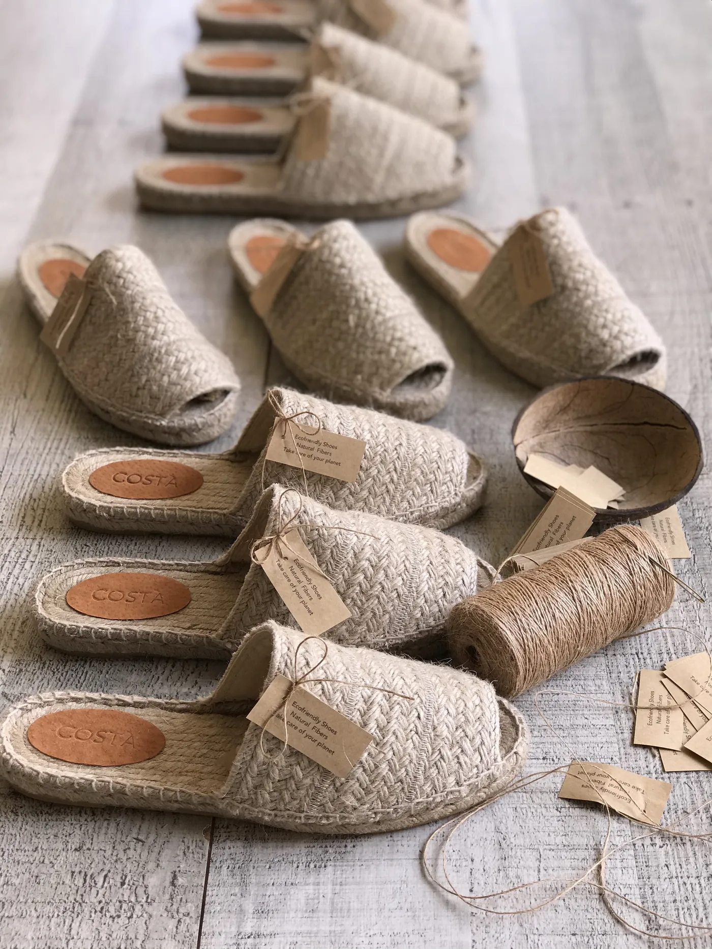 A series of woven mules, tags and a spool of thread on a wooden table.