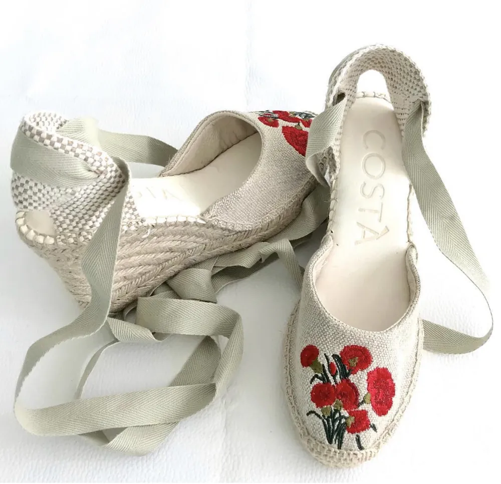 Light-coloured espadrilles with red floral embroidery and tie ribbons.