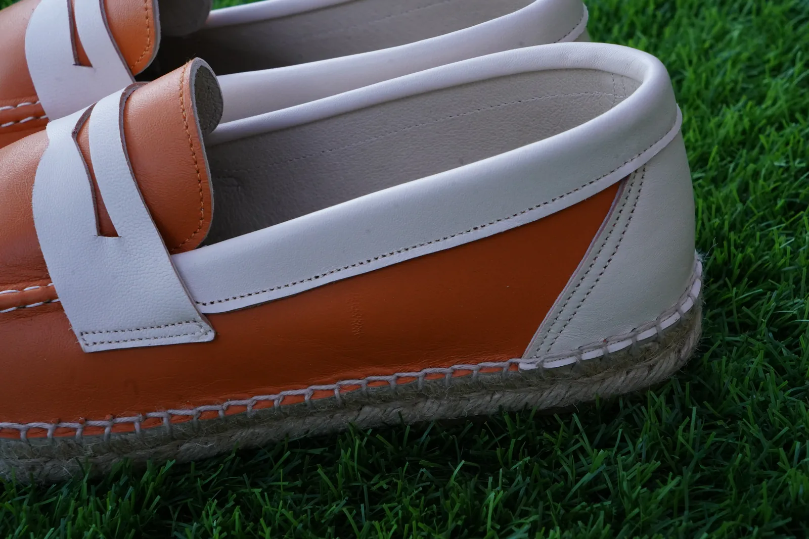 Close-up of an orange and white loafer and its stitching along the rope sole.